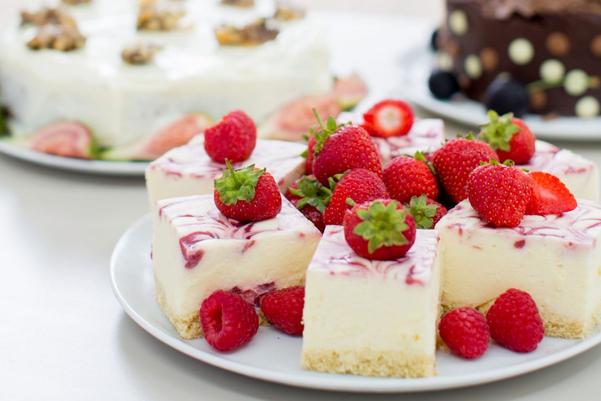 Three cakes on a table in an outdoor setting. One cake has strawberries on it and one is chocolate. The other looks like walnuts are on top.